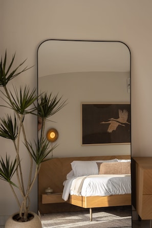 Ein Schlafzimmer mit einem Bett, einem Nachttisch, einem Spiegel, einem Wandbild und einer Zimmerpflanze.