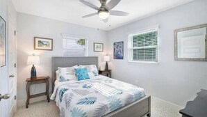 Une chambre à coucher avec un lit, deux tables de chevet, un ventilateur de plafond et des tableaux encadrés accrochés aux murs.