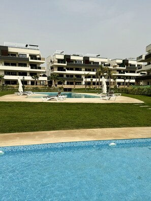 A modern hotel with a swimming pool, multiple balconies, and a well-maintained lawn. - Apartment Playa Flamenca Deluxe (Orihuela)