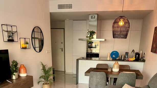 Ein modernes Wohnzimmer mit einem grauen Sofa, einem Couchtisch und einem Essbereich mit Stühlen.