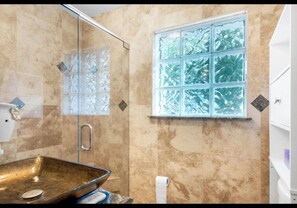 A bathroom with a glass shower enclosure, a sink with a basin, a toilet, and a window with frosted glass panes.