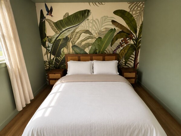 Una cama con cabecera de madera, dos mesitas de noche y un mural con motivos tropicales en la pared.