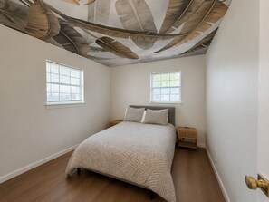 Ein Schlafzimmer mit einem Bett, zwei Nachttischen und einer Decke mit Blättermotiv.