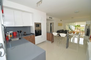 Een moderne keuken met witte kasten, een roestvrijstalen spoelbak en een eethoek met een witte tafel en barstoelen.