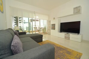 Ein modernes Wohnzimmer mit einem grauen Sofa, einem Flachbildfernseher an einem weißen Schrank und einem gelben Teppich.