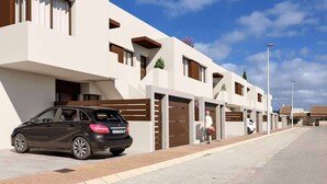 Um edifício residencial moderno com um carro estacionado em frente, céu claro e uma calçada para pedestres.