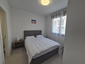 A bedroom with a bed, nightstands, a lamp, a painting, and a window with curtains. - Groundfloor Beliche San Pedro Pinatar (San Pedro del Pinatar)