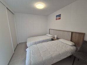 Una habitación de hotel con dos camas, una mesita de noche, una lámpara y un cuadro en la pared.