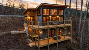 Een houten chalet met twee verdiepingen, een balkon, grote ramen en een terras.