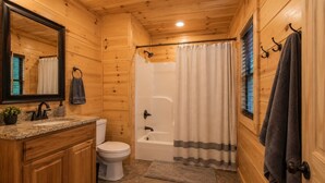 Een houten badkamer in een chalet, met een wastafel, toilet, bad en douchegordijn.