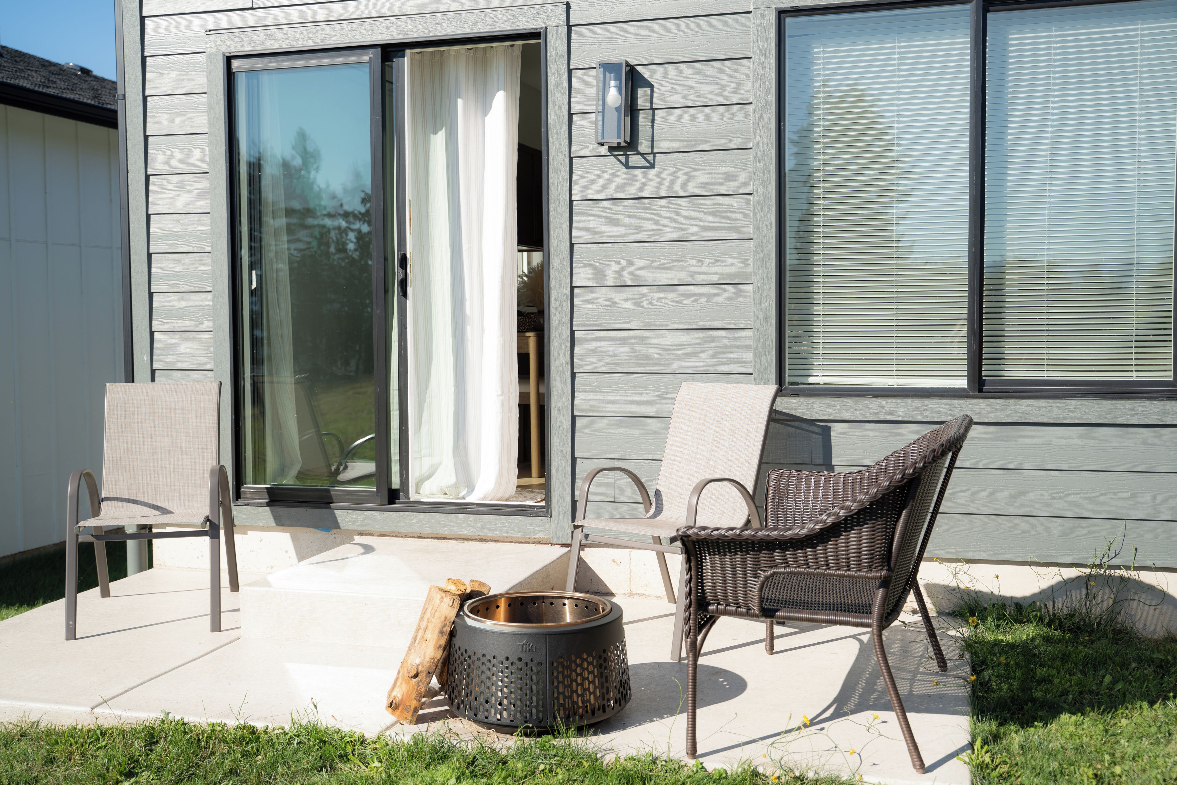Een terras met een rieten stoel, een metalen tafel en een vuurkorf.
