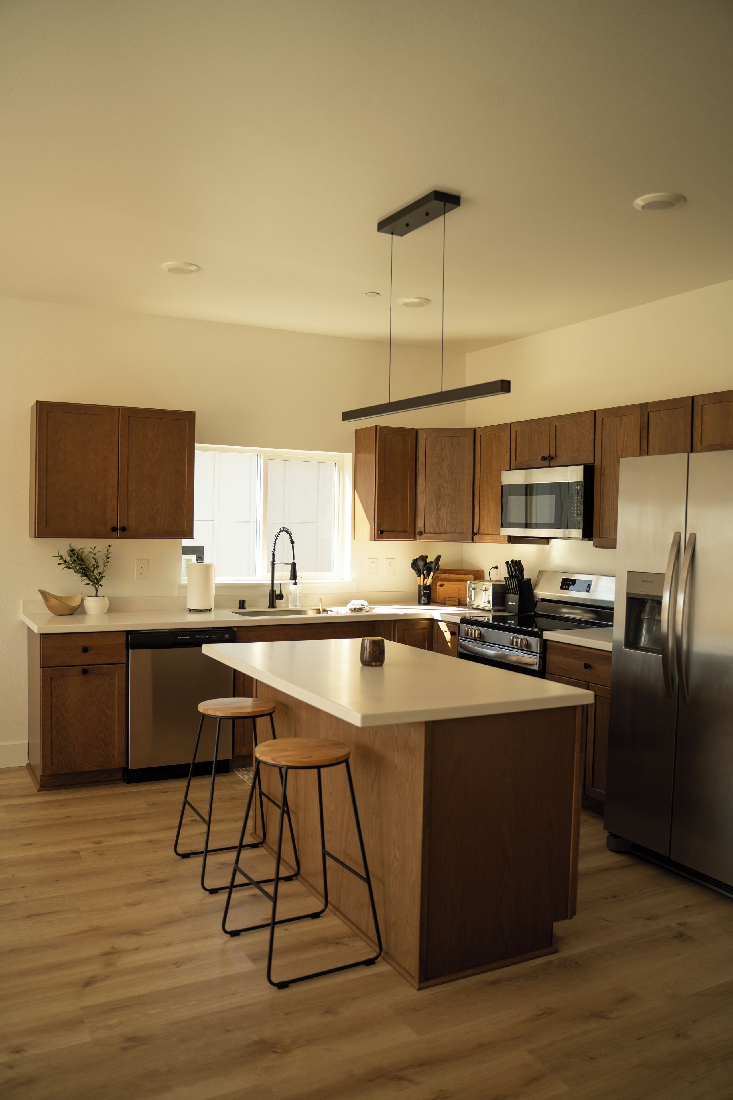 A modern kitchen with wooden cabinets, a stainless steel refrigerator, and a central island with stools.