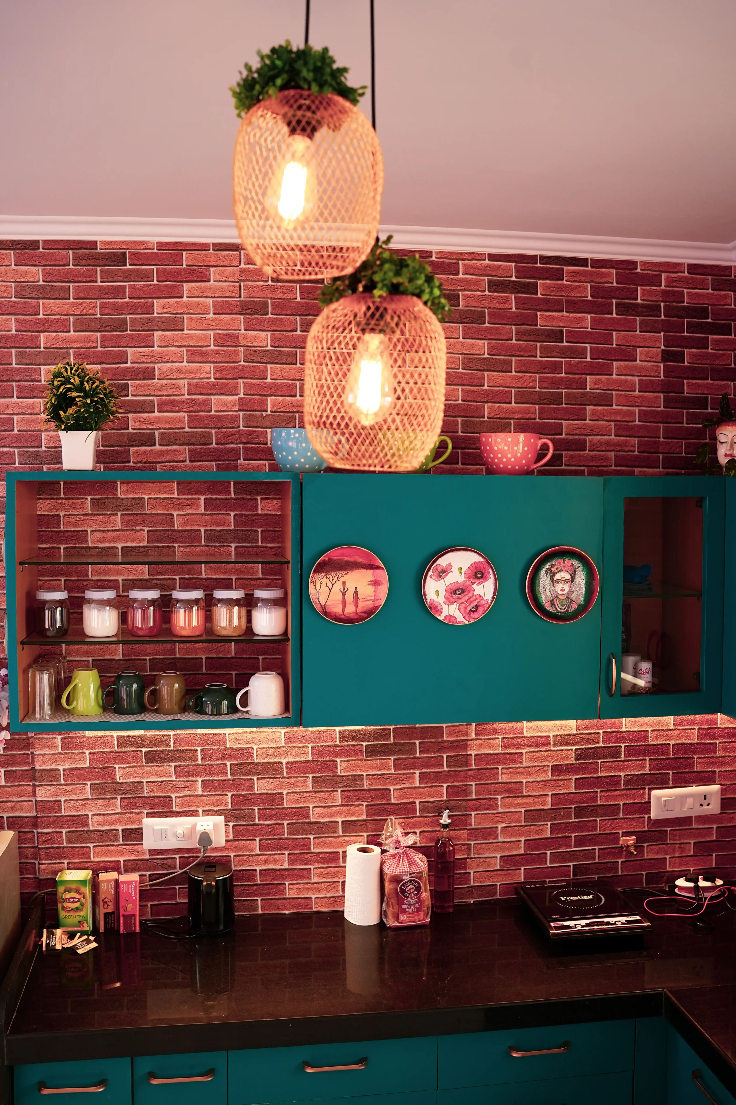 Une cuisine avec un mur en briques, des armoires de couleur turquoise, des luminaires suspendus en osier et une variété d’ustensiles de cuisine.