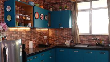 A kitchen with blue cabinets, a stainless steel refrigerator, a brick backsplash, and hanging pendant lights.