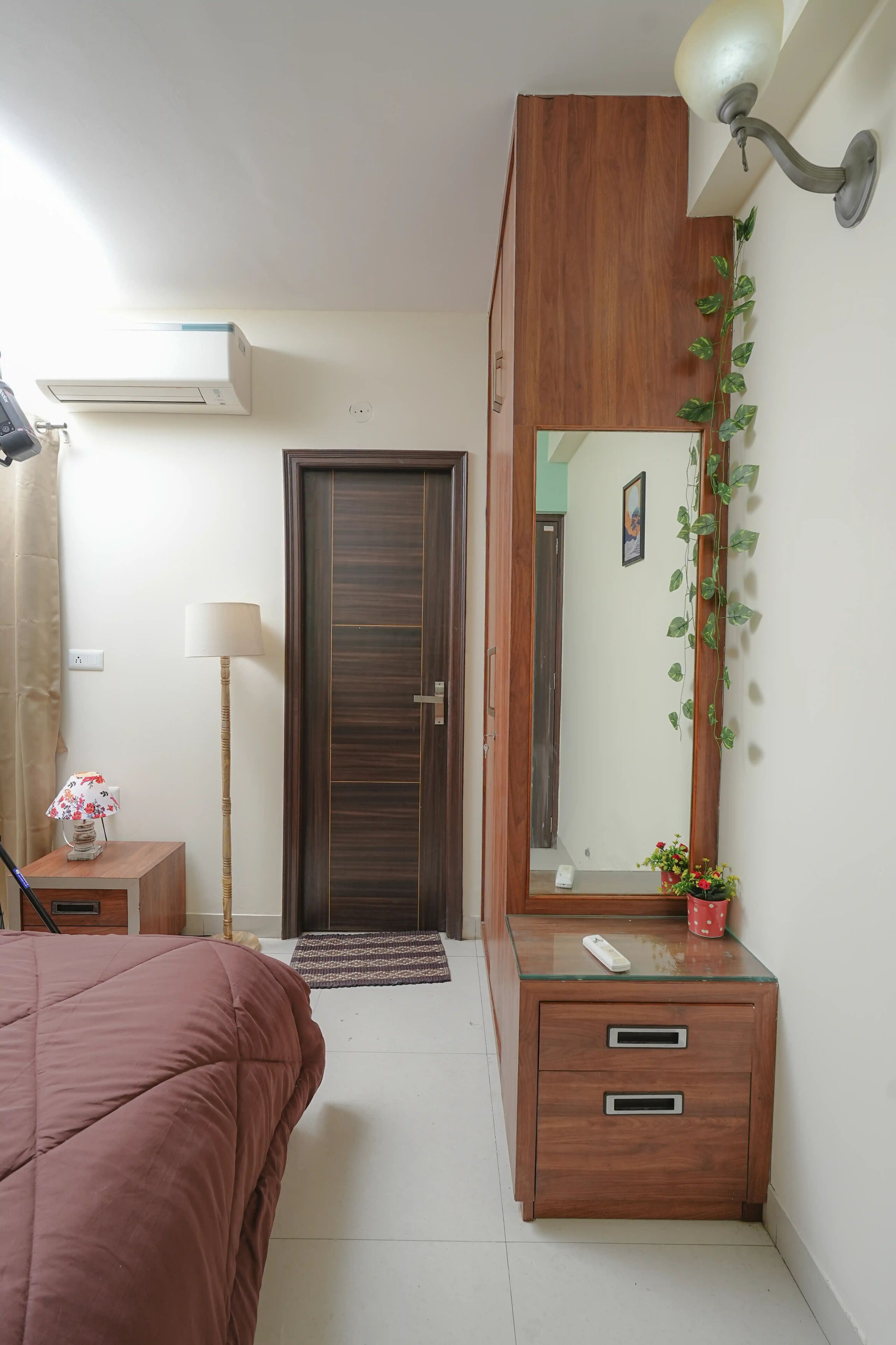 A bedroom with a bed, a bedside table with a lamp, a dresser with a mirror, and a door.