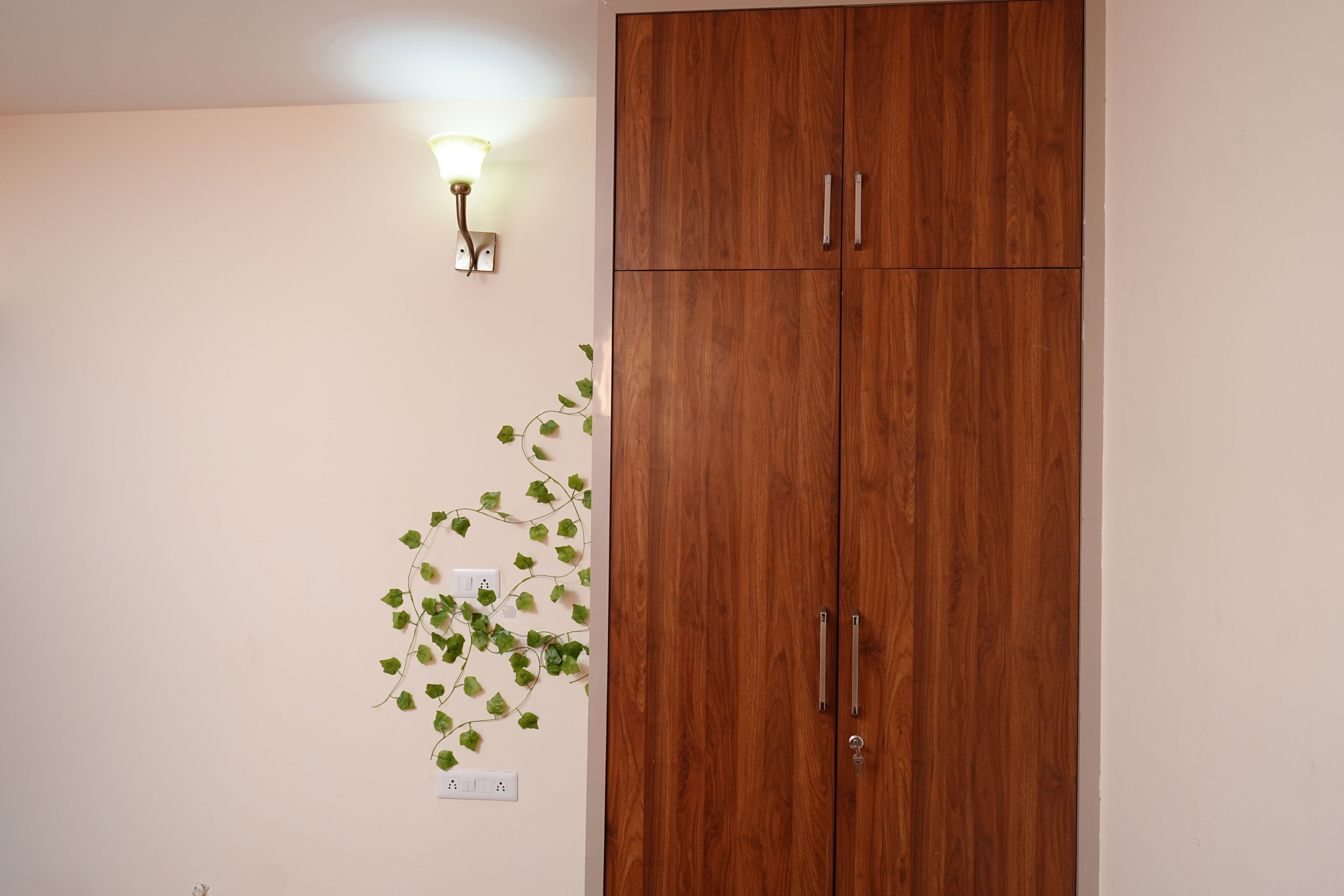 A wooden wardrobe with two doors and a wall-mounted light fixture.