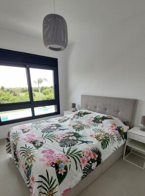 A bedroom with a bed, a window, a bedside table, and a hanging light fixture. - Penthouse Romerogolf (Pilar de la Horadada)