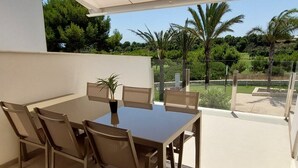 Un espacio de comedor al aire libre con techo, una mesa, sillas, una planta en maceta y vistas a follaje y árboles.
