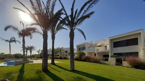Una casa moderna de dos pisos con piscina, rodeada de césped cuidado y palmeras.