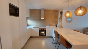 Una cocina moderna con horno empotrado, microondas y campana extractora. Hay una mesa de comedor con sillas y lámparas colgantes arriba.