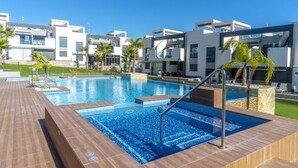 A modern hotel with a swimming pool, outdoor seating, and a clear blue sky. - Penthouse Oasis Beach IX Punta Prima (Torrevieja)