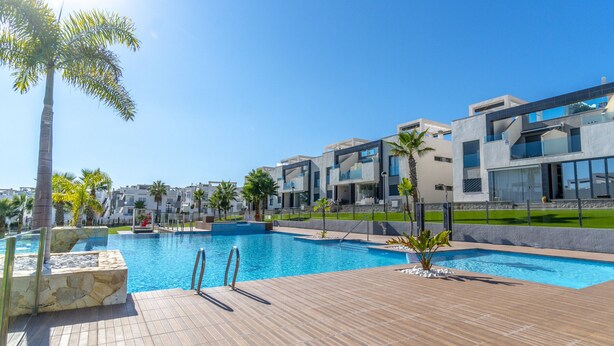 A modern hotel with a swimming pool, palm trees, and a clear blue sky. - Penthouse Oasis Beach IX Punta Prima (Torrevieja)