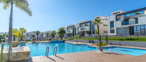 A modern hotel with a swimming pool, palm trees, and a clear blue sky.