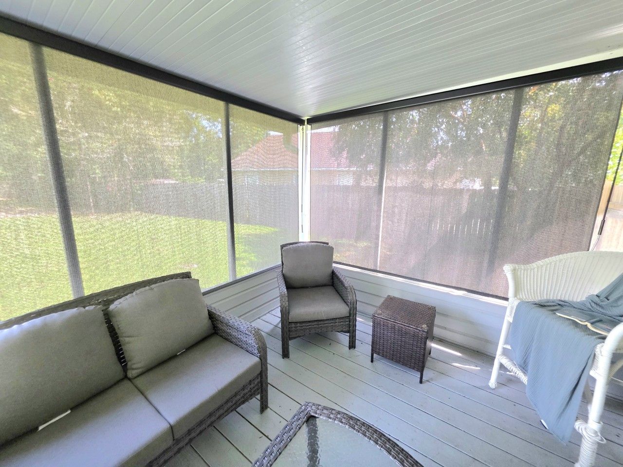 A screened porch with a sofa, chairs, and a small table.