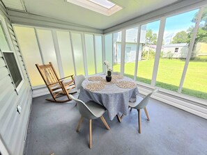 A sunroom with a table and chairs, large windows, and a view of a yard.