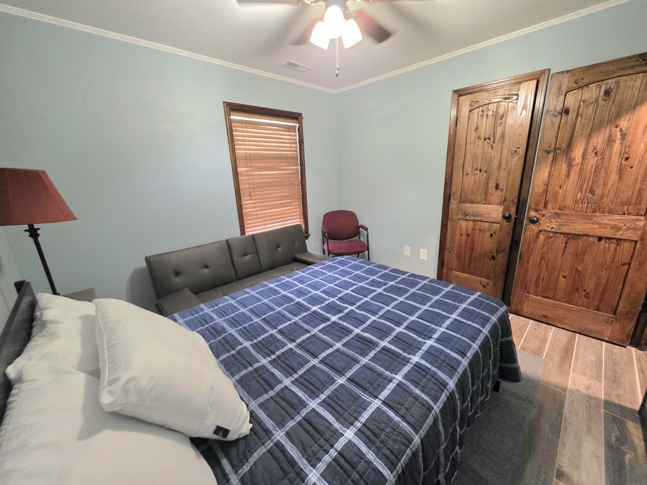 Un dormitorio con cama, una silla, armario y ventilador de techo.