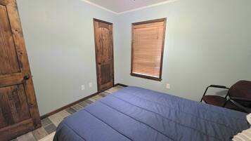 A bedroom with a bed, two doors, a window with blinds, a chair, and a ceiling fan.