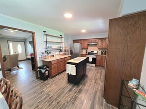 A modern kitchen with wooden cabinets, a central island, and a dining area with a chair.