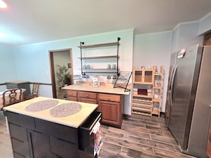 A kitchen with a central island, wooden cabinets, a stainless steel refrigerator, and a hanging shelf above the island.