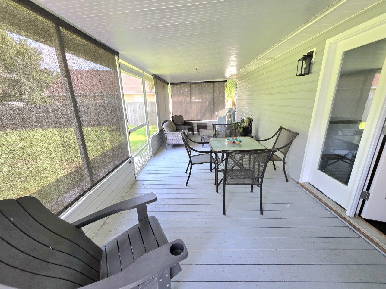 Eine überdachte Veranda mit Tisch und Stühlen, eine Schiebetür aus Glas und Blick ins Freie.