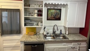 A kitchen with white cabinets, a double sink, a dishwasher, and a painting above the sink. - Desert Rose Located Near Texas Tech (Lubbock)