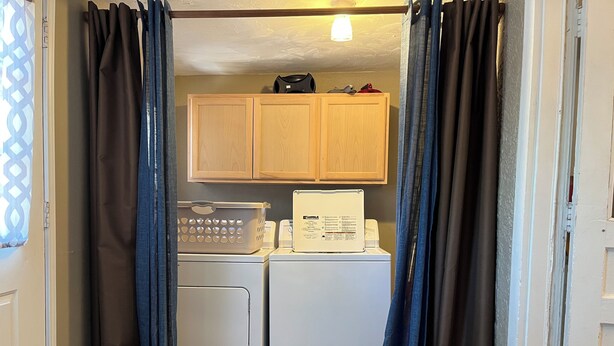 A laundry area with a washing machine, dryer, and wooden cabinets above. - Desert Rose Located Near Texas Tech (Lubbock)