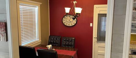 A dining area with a red wall, a clock, and a chandelier.