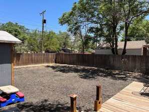 Ein Garten mit einer Holzterrasse, einem eingezäunten Bereich und einer kleinen Spielanlage.
