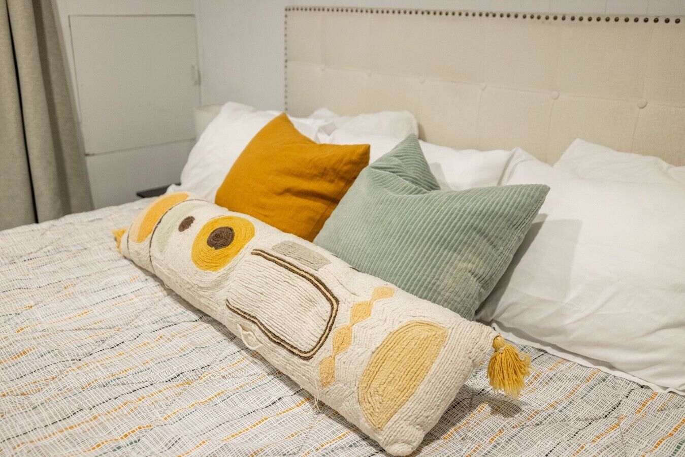 A bed with a patterned bedspread, multiple pillows, and a decorative pillow with a tassel.