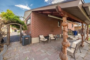A covered outdoor seating area with brick walls, a pergola, and a sculpture. - Cozy Stay | Patio | Full Kitchen | Long Term Ready (Sandy)