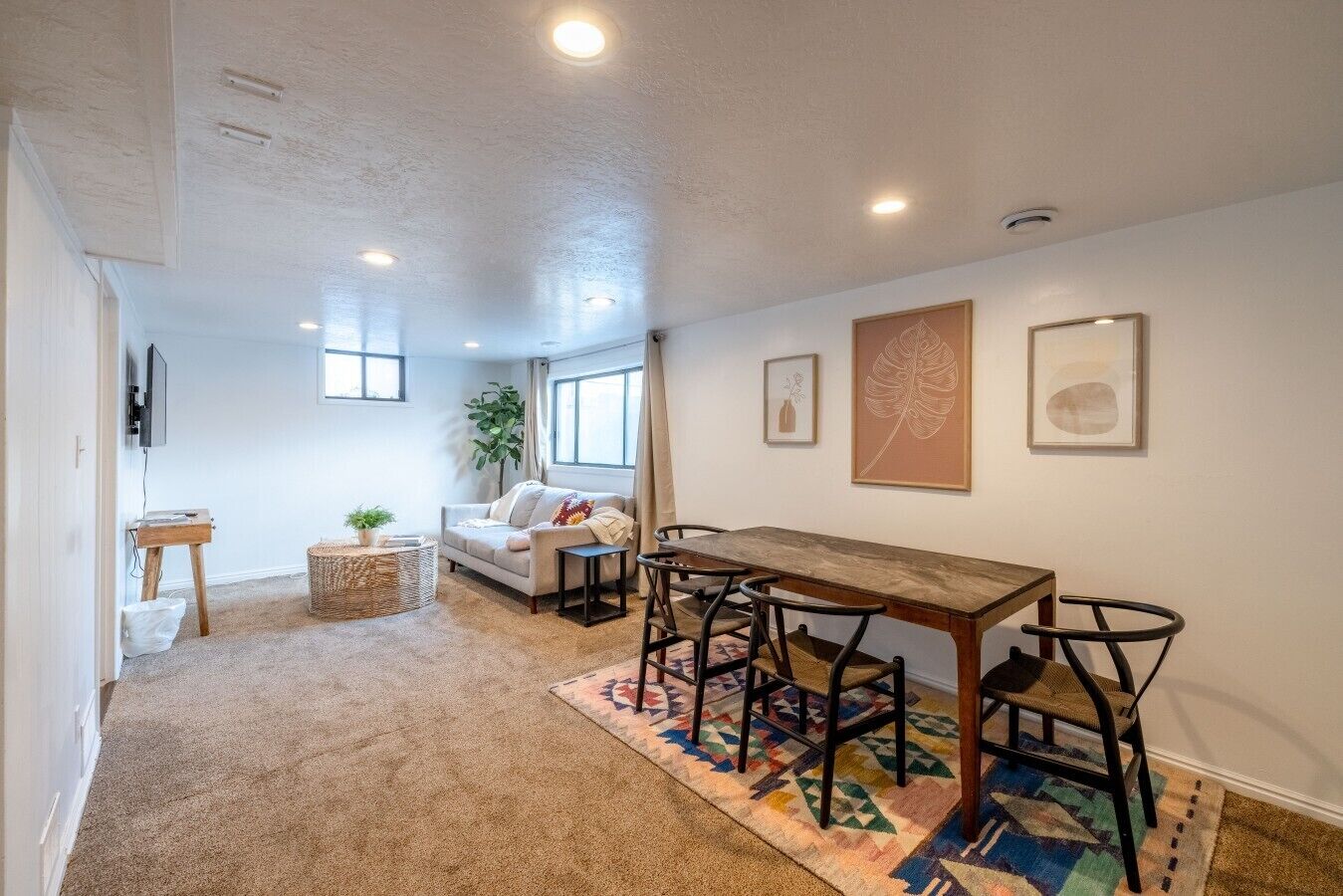 A room with a wooden dining table, four chairs, a sofa, a TV, and artwork on the walls.