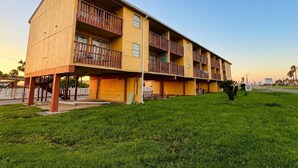 A multi-story building with balconies, a grassy area in front, and a clear sky. - Oro North Beach Inn (Corpus Christi)