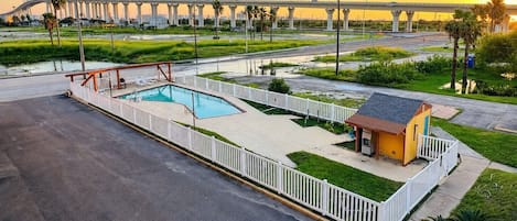 A swimming pool with a deck, a small building, and a bridge in the background.