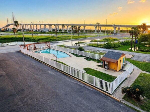 A swimming pool with a deck, a small building, and a bridge in the background.