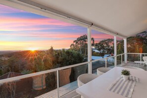 Un balcón con vista al atardecer, muebles blancos y una planta en maceta.