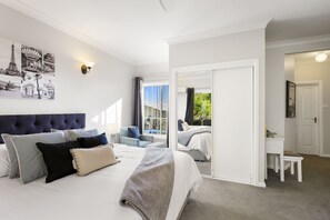 Un dormitorio con una cama grande, una silla, un escritorio y vistas al exterior.