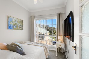 Un dormitorio con cama, escritorio, televisor y ventana con cortinas.