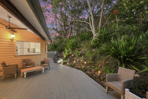 Una terraza de madera con mobiliario exterior, rodeada de vegetación exuberante y vistas a árboles.