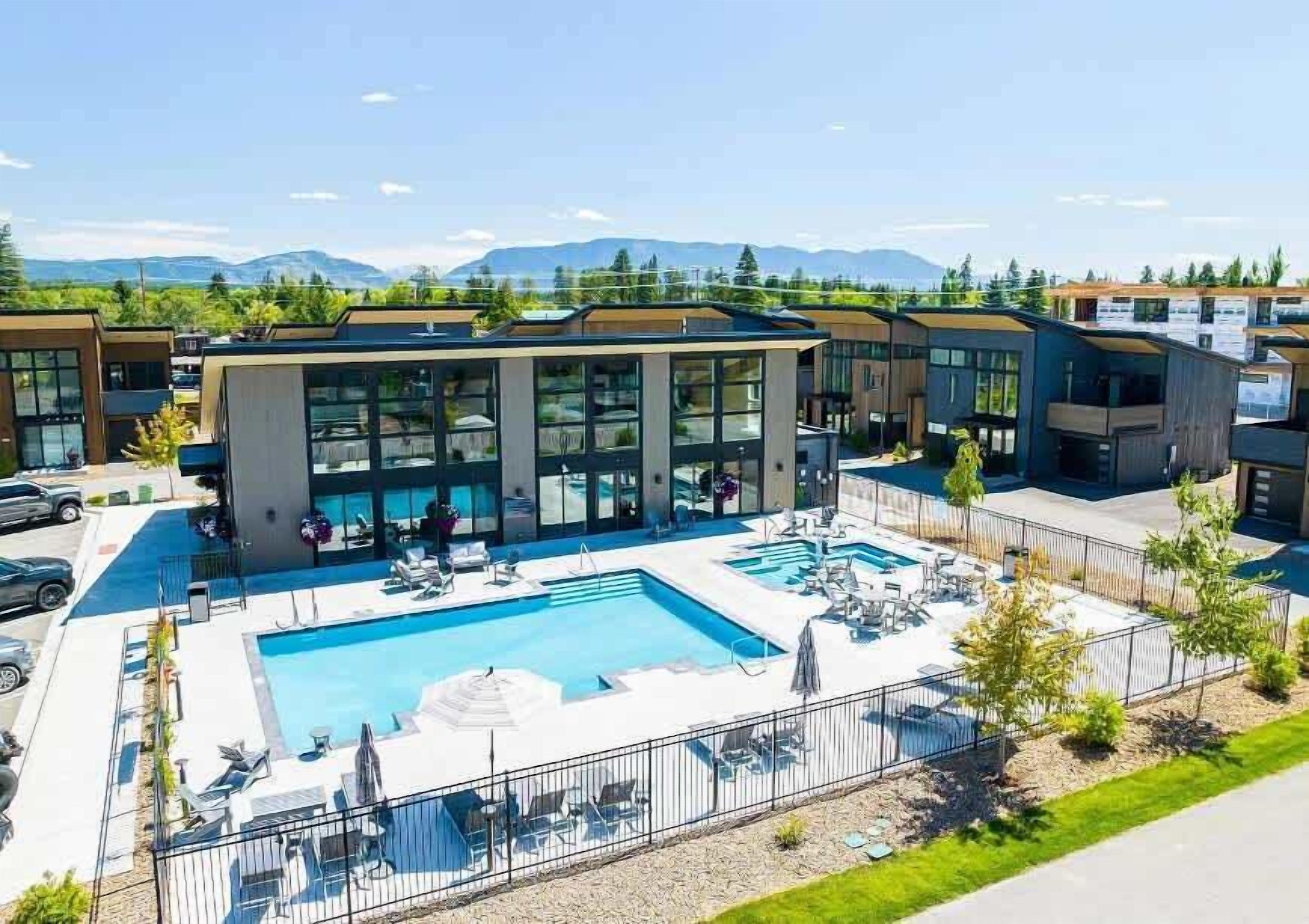 A modern hotel with a swimming pool, lounge chairs, and a view of mountains.