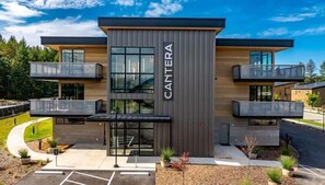 A modern building with a name sign, multiple balconies, and a parking area. - Clubhouse & Pool Amenities, 40 Mins to Glacier NP (Whitefish)